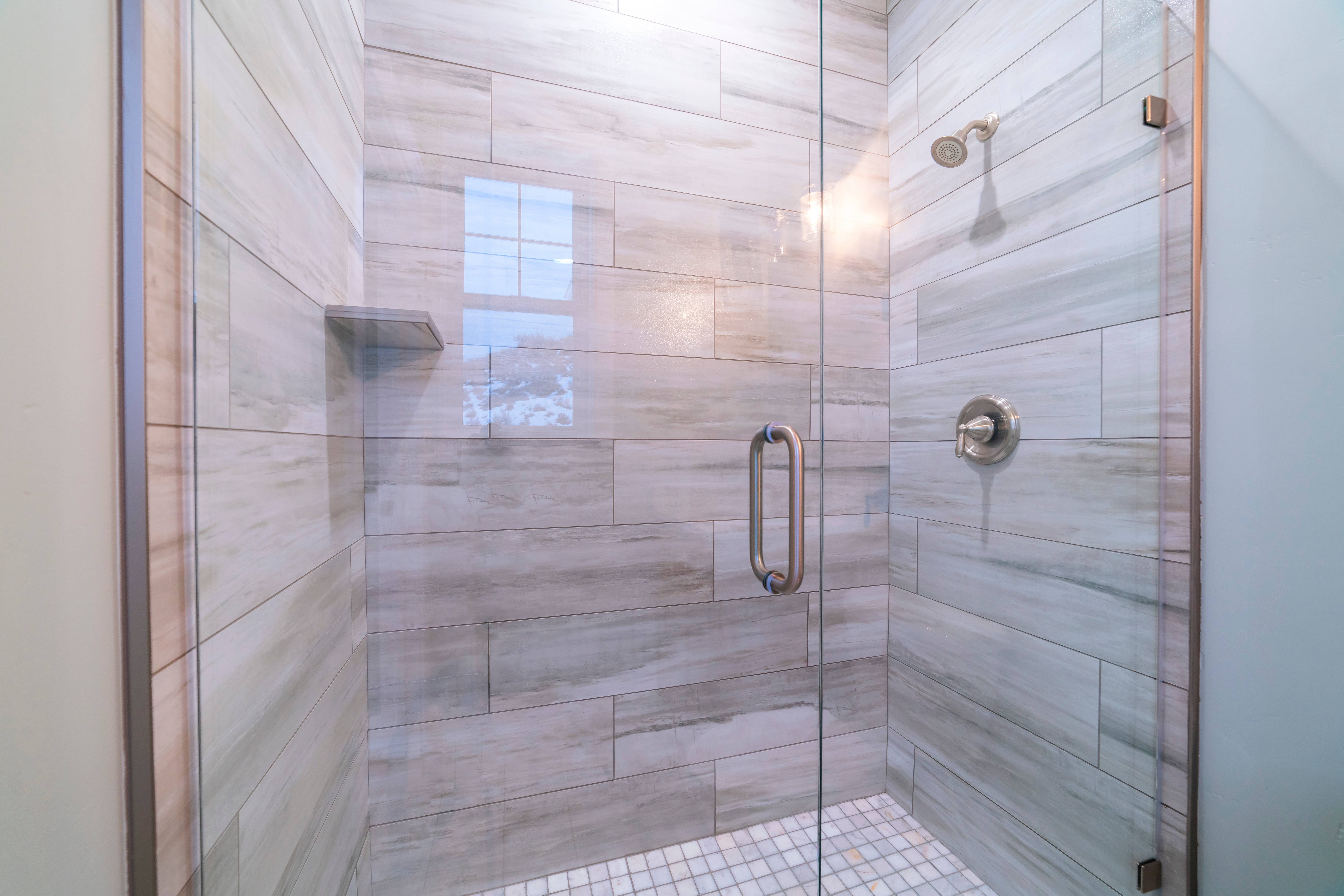 White and gray large tiles in new shower with glass door