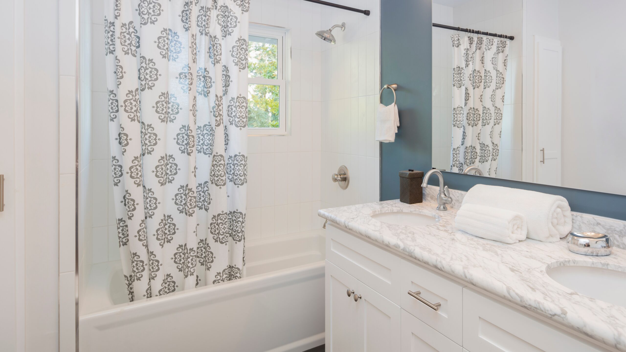 A white bathroom with a white bathtub and detailed shower curtain