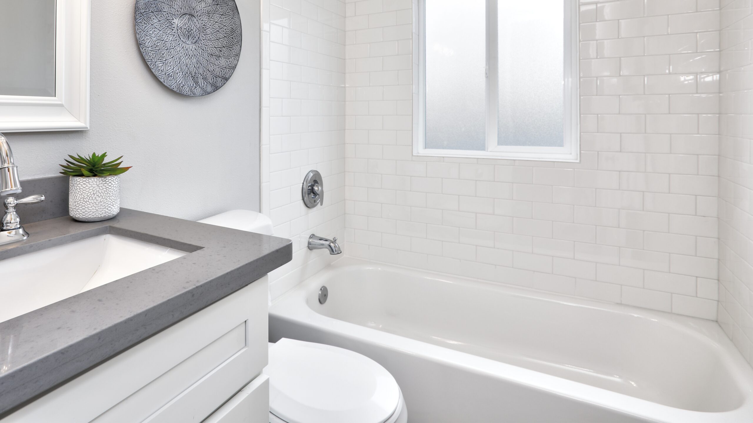 A bathroom with white walls and a white tub with a window