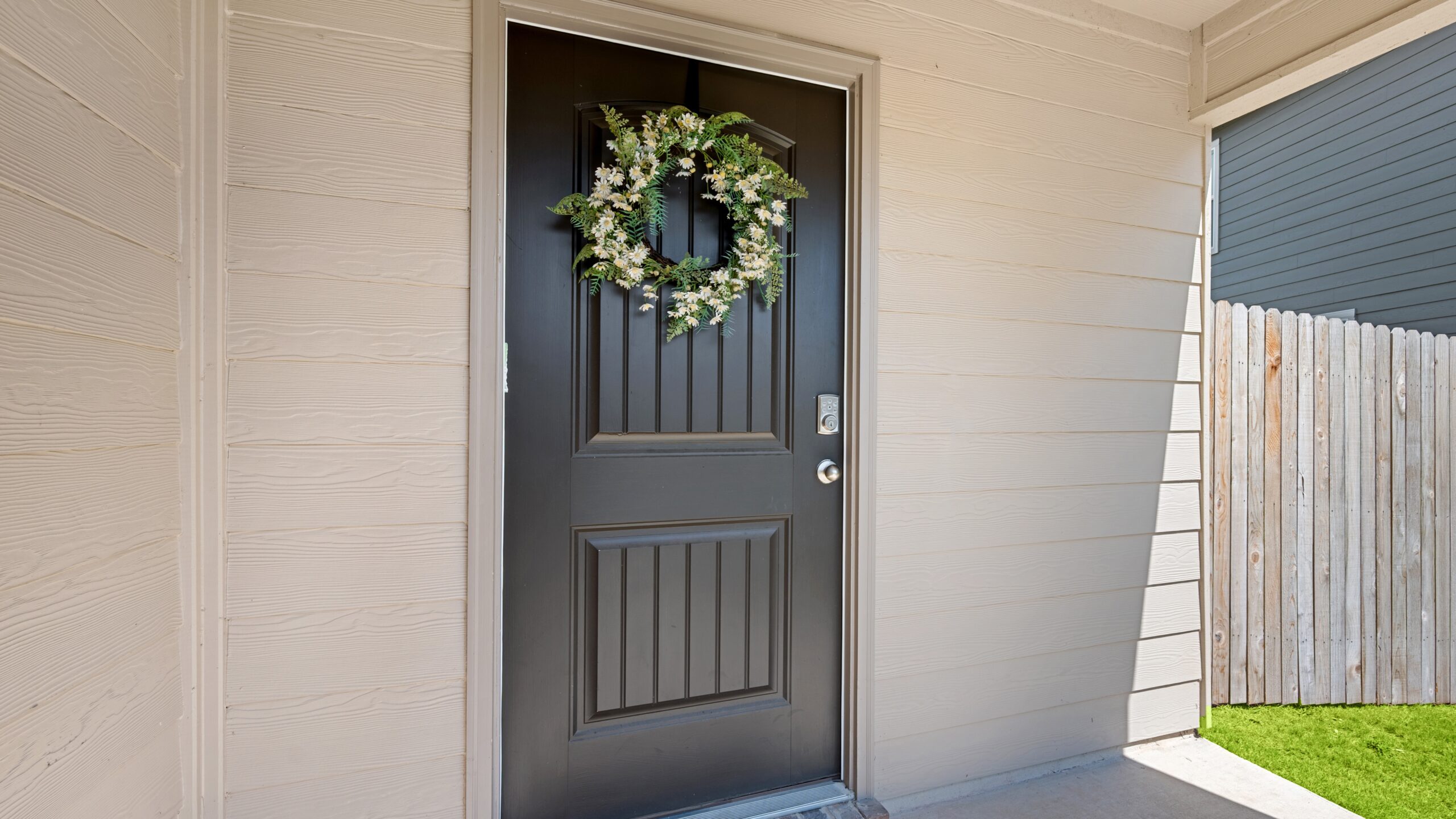 A black entry door with a green wreath in a home with white siding