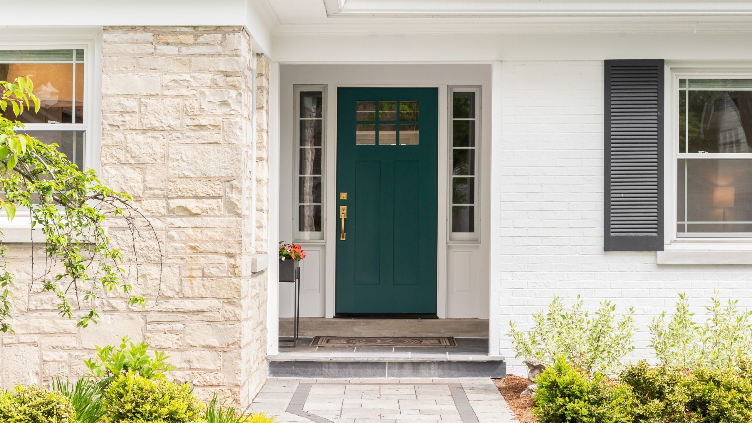 A green door in a home with white siding and stone columns