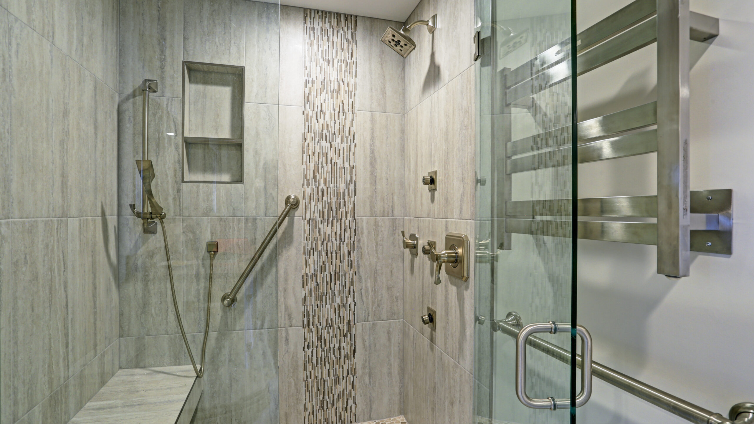 A walk-in shower with gray wall surrounds, grab bars, and built-in shelving